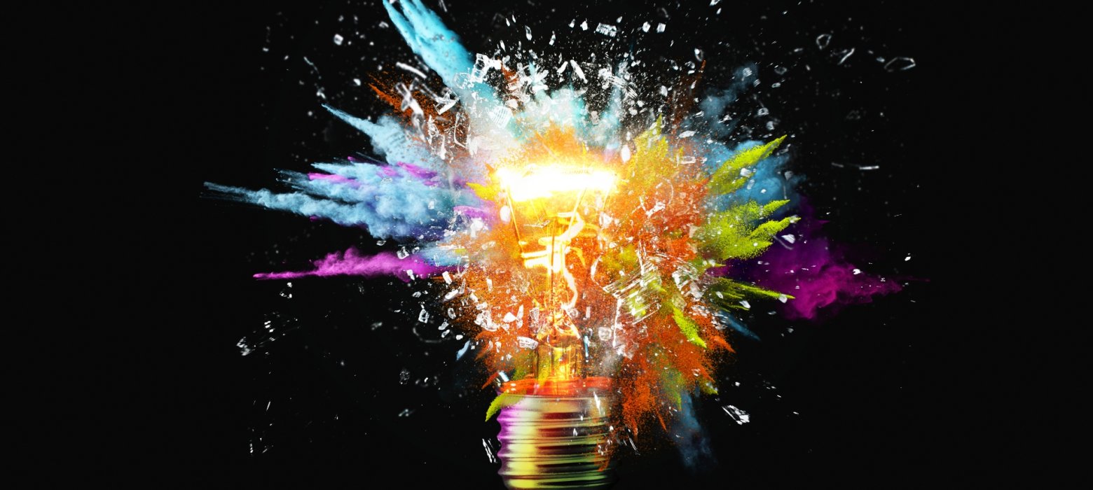 Creative light bulb explodes with colorful paint splashes and shards of glass on a black background. Think differently creative idea concept. Dry paint splatter. Brainstorm and think